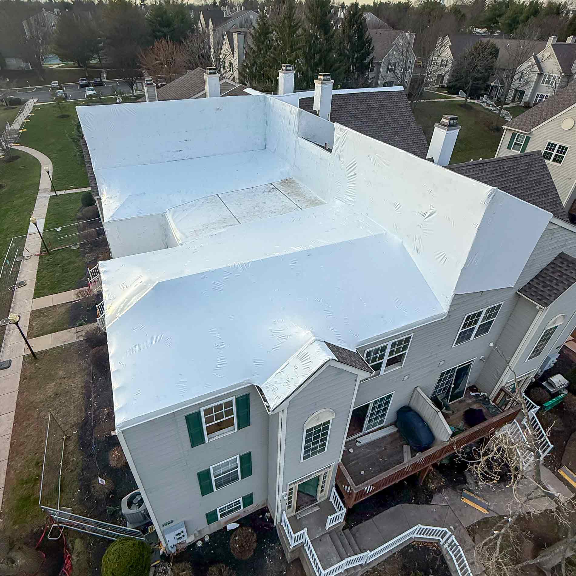 Aerial view of a white flat roofed residential building with a small open rooftop area surrounded by neighboring houses and trees