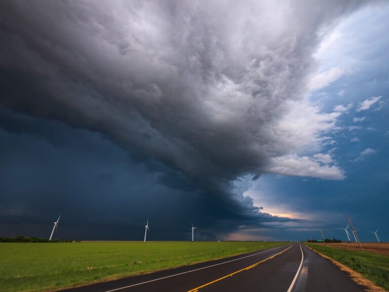 devastating effects severe storms communities StormWrappers StormWrappers Dark storm clouds loom over a flat rural landscape with wind turbines and a long empty road ahead