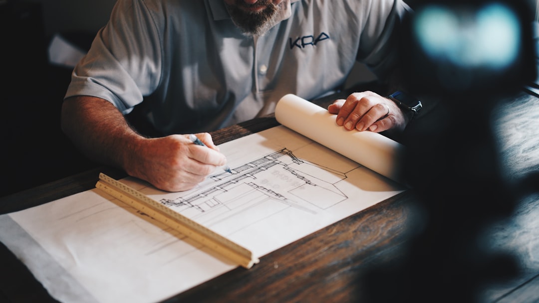 Engineer or architect drafting a building plan on blueprints at a wooden table, using a pencil and ruler