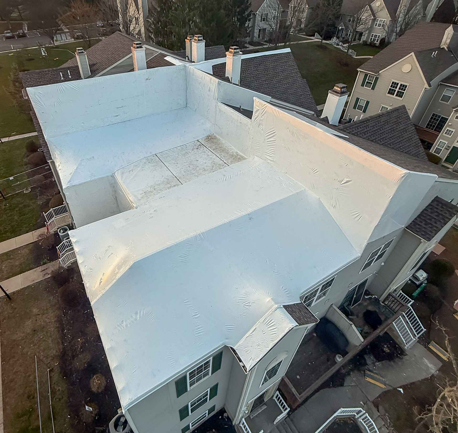 Aerial view of a white coated flat rooftop with several chimneys and nearby townhomes visible