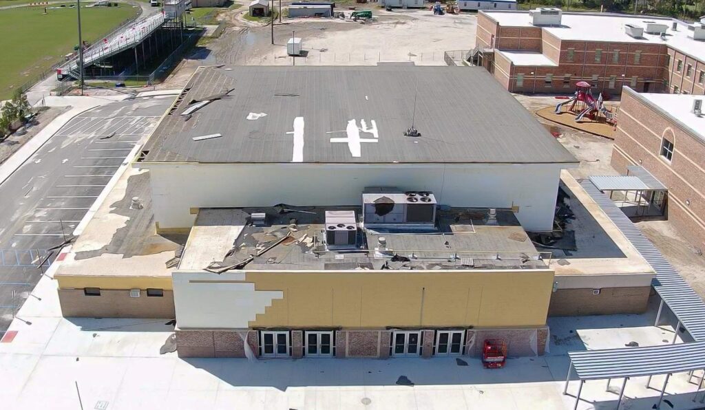 Aerial view of a school building with a damaged roof hvac units and loose roofing material a playground is visible nearby