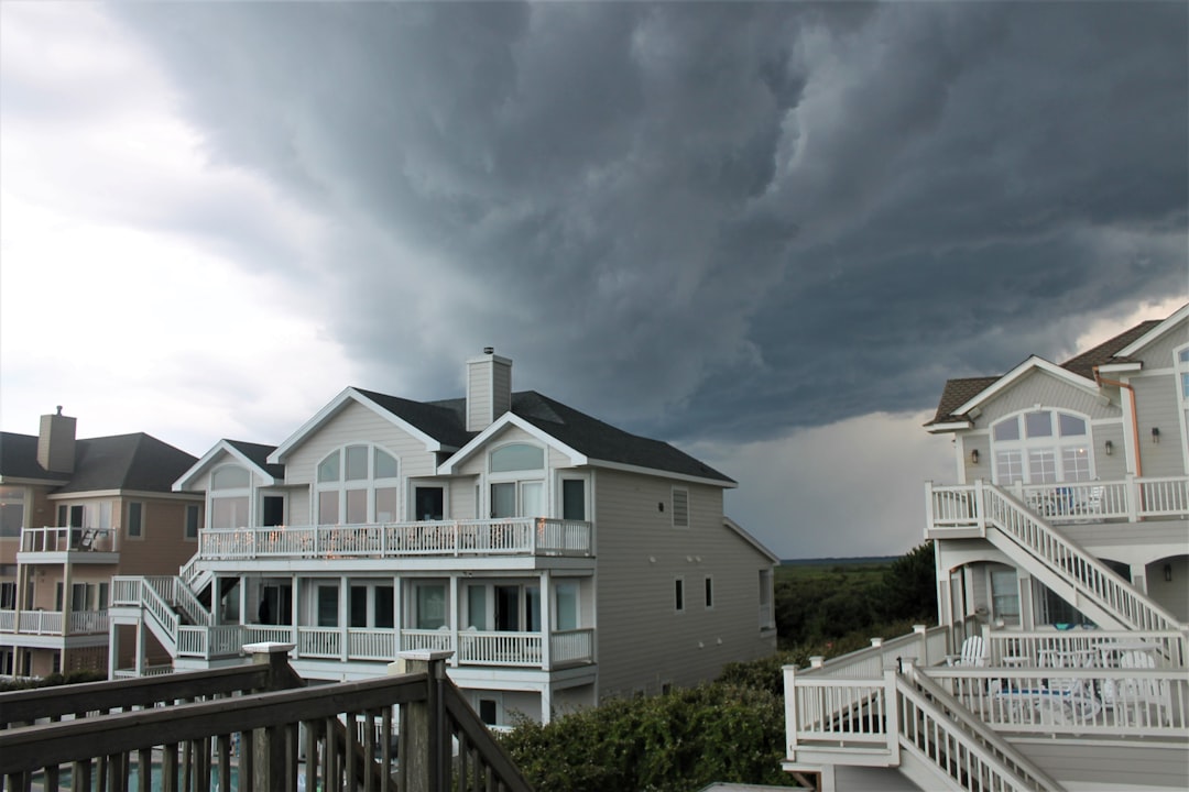 Row of light-colored beachfront townhouses with white railings under a looming dark storm cloud.] , sorry