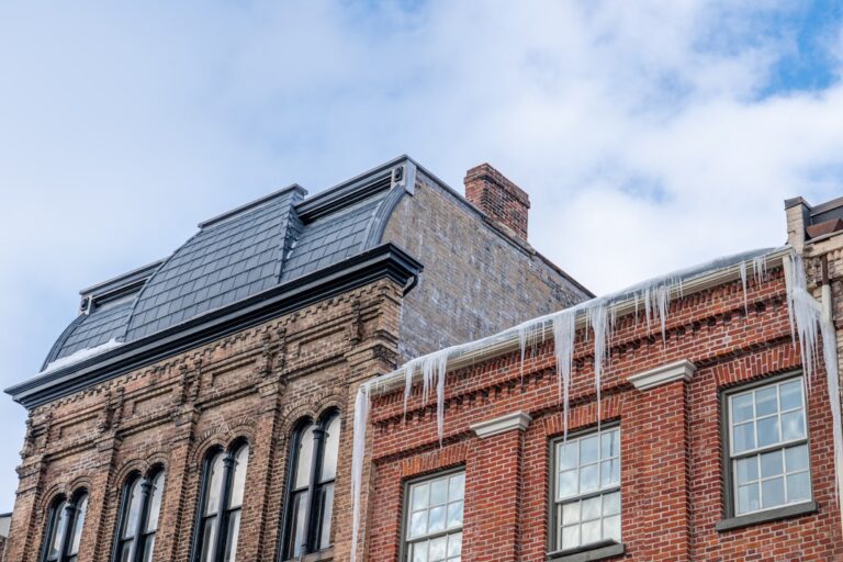 top roofing materials prevent ice dams StormWrappers StormWrappers Historic brick building with arched windows and hanging icicles along the roofline against a blue sky